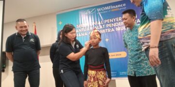 Cincin Lisa Hadi, Direktur WOM Finance memasang salah alat bantu pendengaran kepada salah satu anak penyandang disabilitas sensorik (tuna rungu)